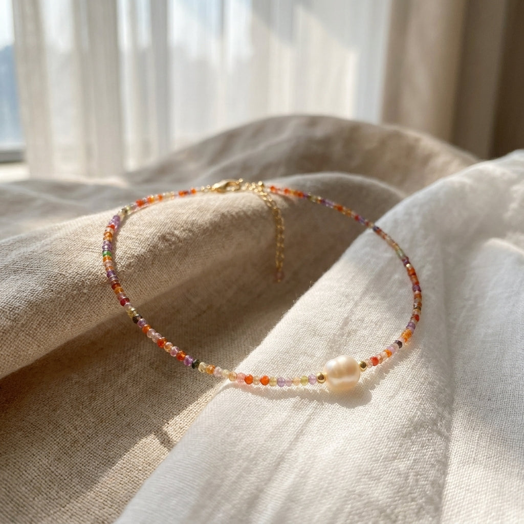 Sunrise Whisper dainty colorful beaded necklace with a central freshwater pearl, delicately resting on textured linen in warm sunlight by Whisperland Studio.