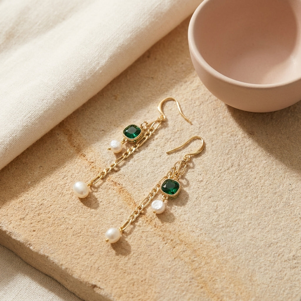 “Verdant Muse” Emerald and Freshwater Pearl Drop Earrings on a textured stone surface with a minimalist ceramic bowl