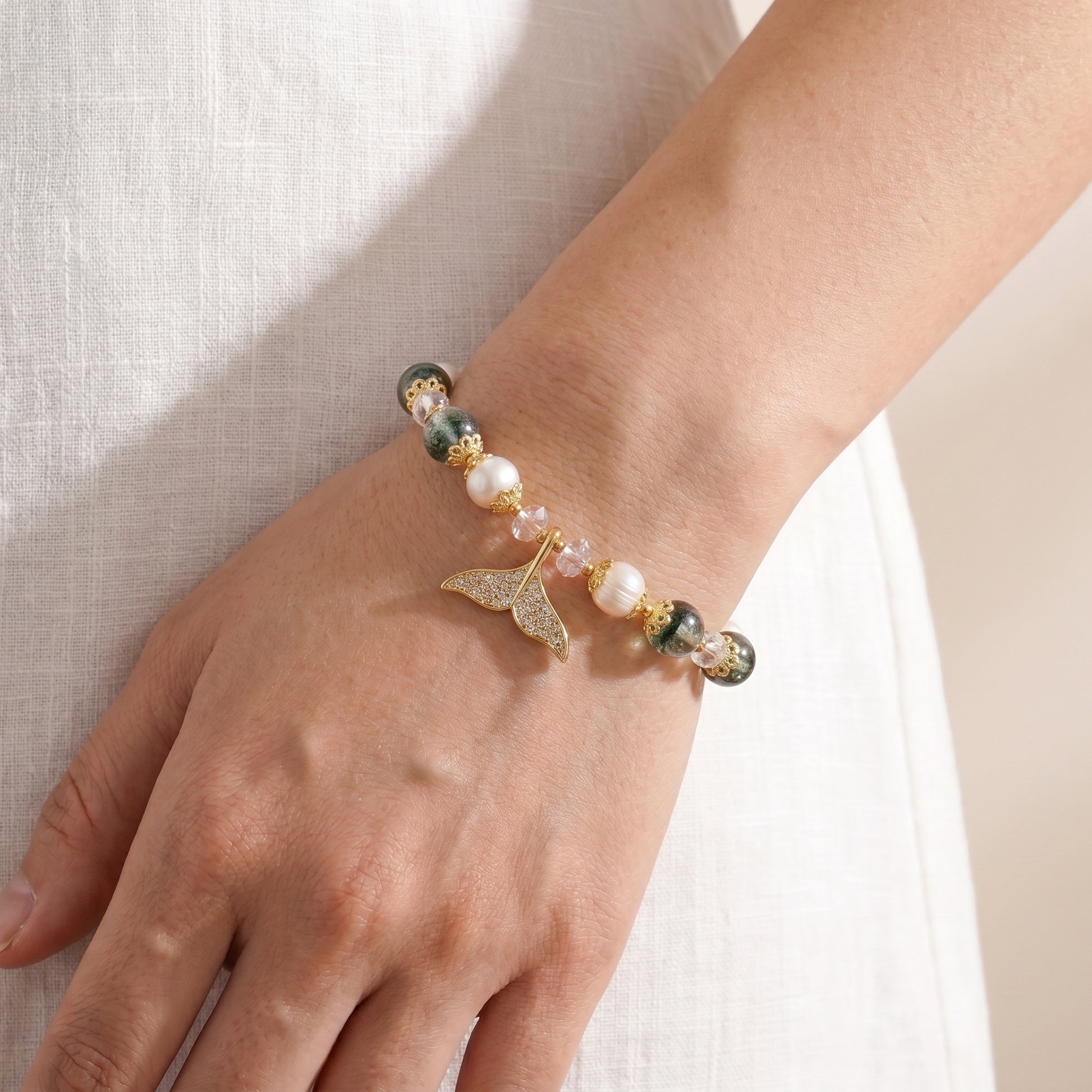 Lifestyle photo showing a person's hands crossed, showcasing the minimalist pearl and green quartz bracelet on their wrist.