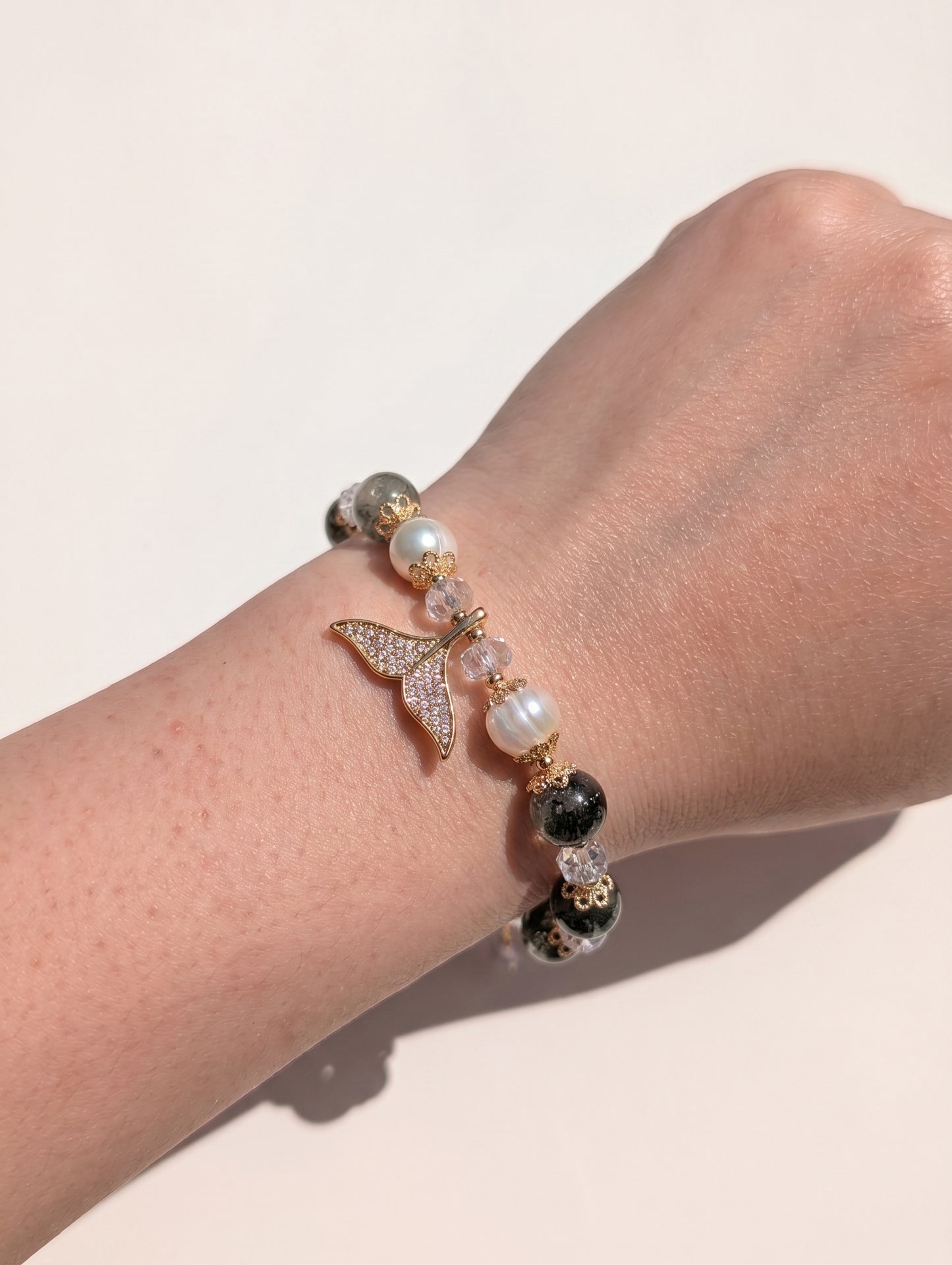A delicate view of the mermaid tail bracelet worn on a wrist, with the hand gently resting against a soft, neutral-toned fabric.
