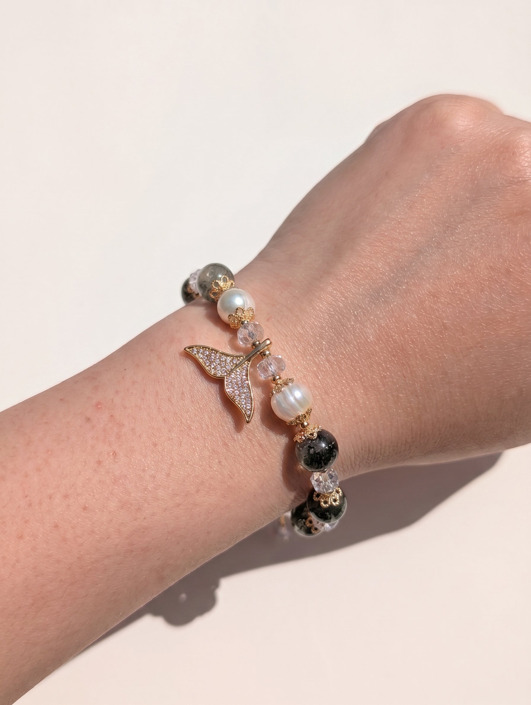 A delicate view of the mermaid tail bracelet worn on a wrist, with the hand gently resting against a soft, neutral-toned fabric.