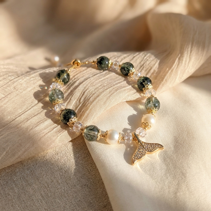 Close-up of the Ocean Reverie bracelet featuring green phantom quartz, white crystals, and freshwater pearls resting on a wavy, sand-like surface.