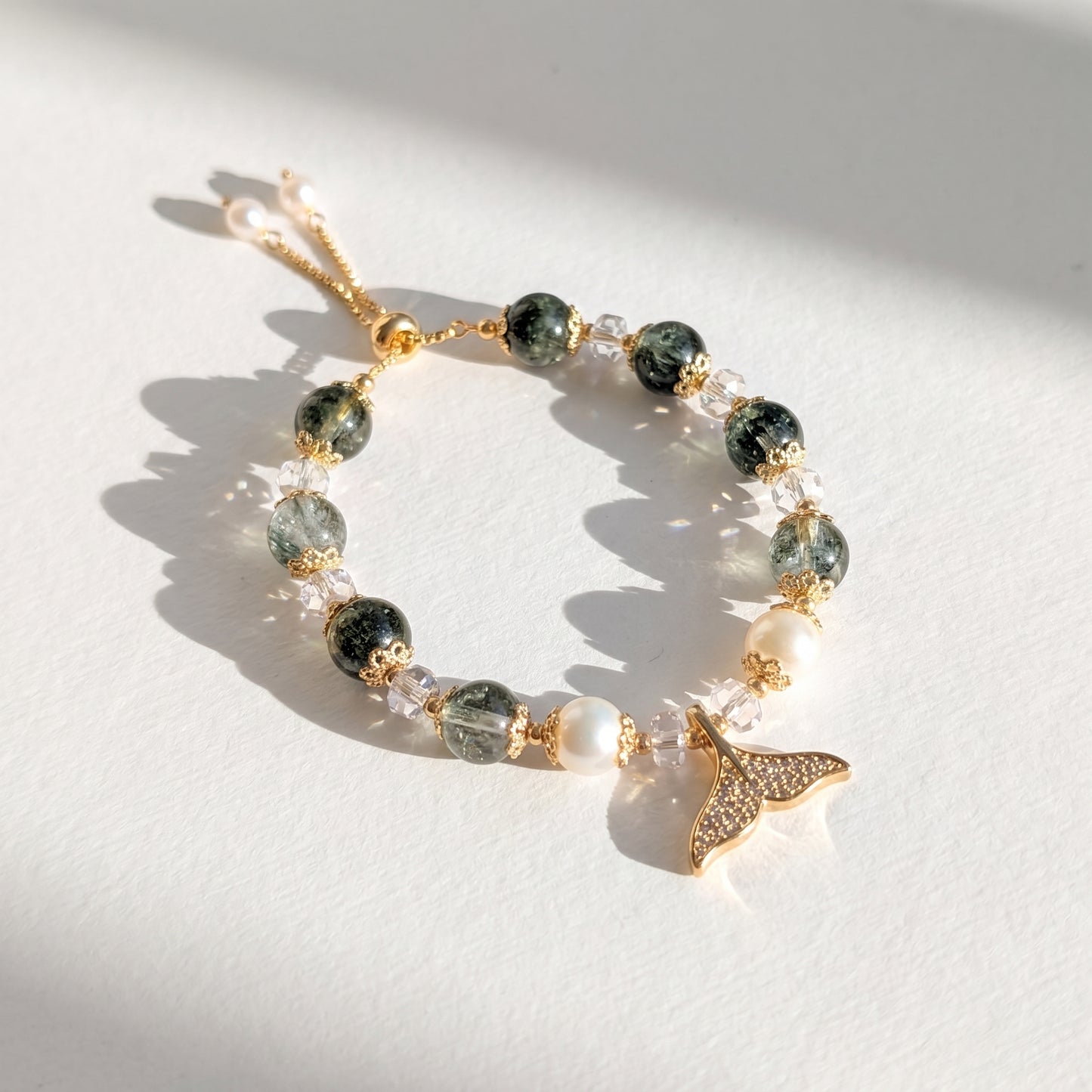The Ocean Reverie Mermaid Bracelet displayed elegantly on a small, white textured block, highlighting the 14K gold-plated cubic zirconia fishtail charm.