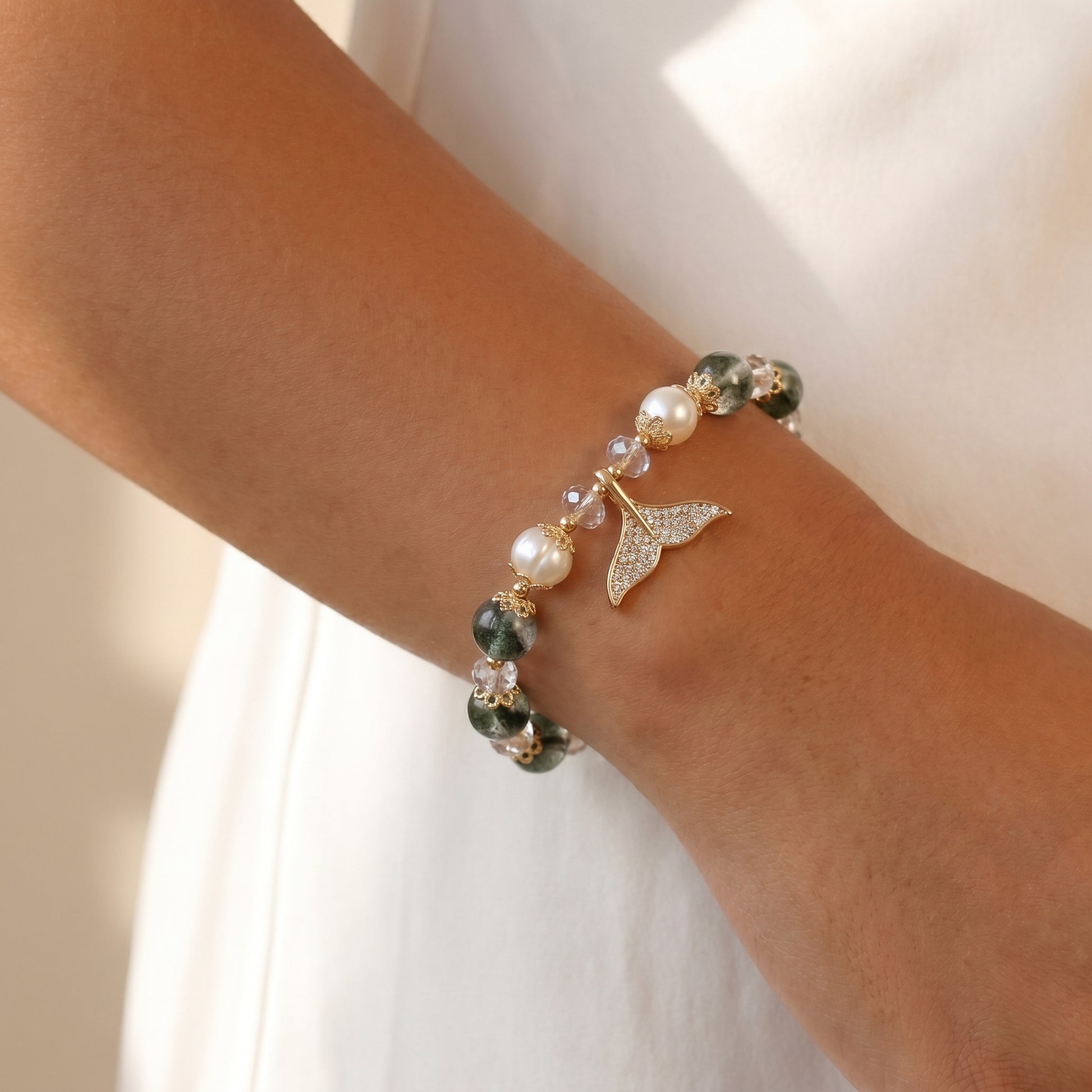 Lifestyle shot of a person's wrist wearing the green quartz and pearl mermaid bracelet, holding a white textured object in soft lighting.
