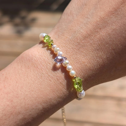 Close-up of a wrist wearing a bracelet with green beads and pearls against a blurred natural background