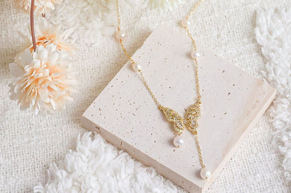 Mariposa gold butterfly pearl drop necklace displayed with a white flower, romantic bridesmaid gift