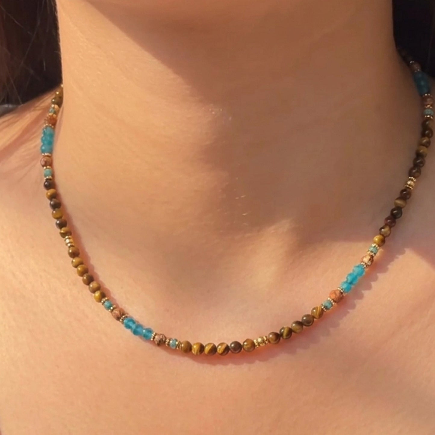 Artisanal gemstone choker featuring natural tiger's eye, blue apatite, and sandstone held delicately by hand.