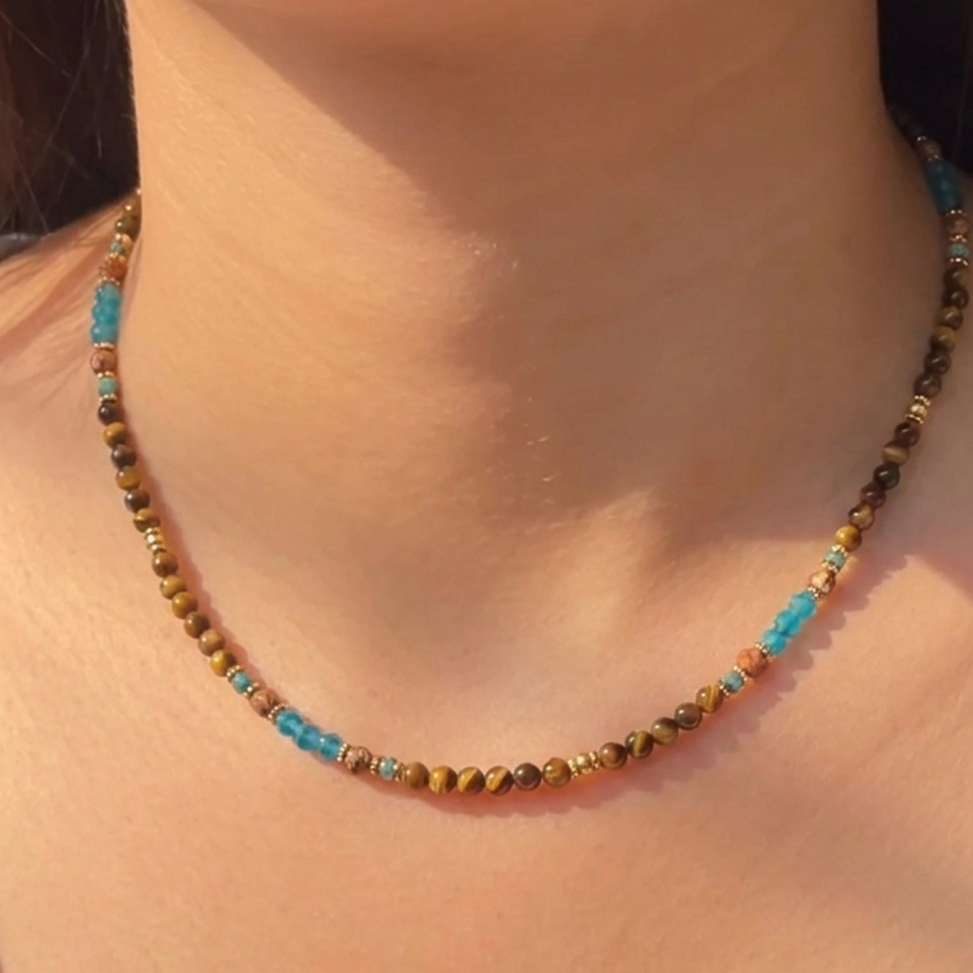 Artisanal gemstone choker featuring natural tiger's eye, blue apatite, and sandstone held delicately by hand.
