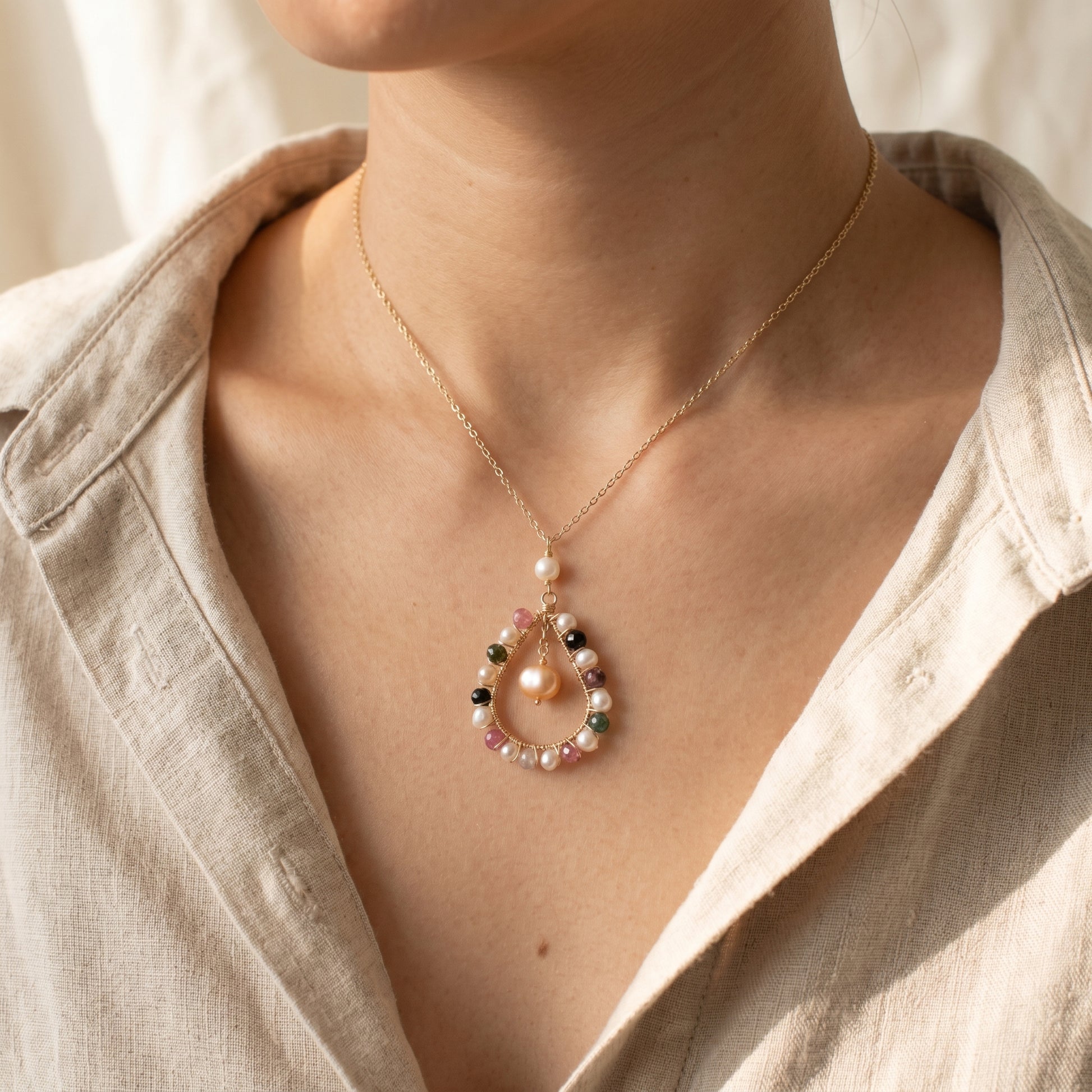 Necklace with a pendant featuring pearls and gemstones worn by a person.