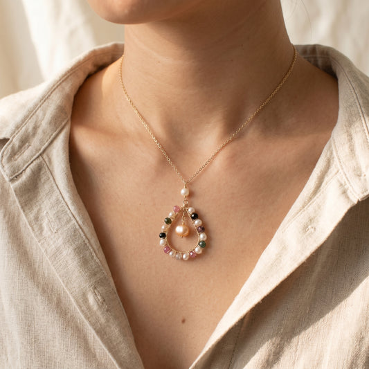 Necklace with a pendant featuring pearls and gemstones worn by a person.