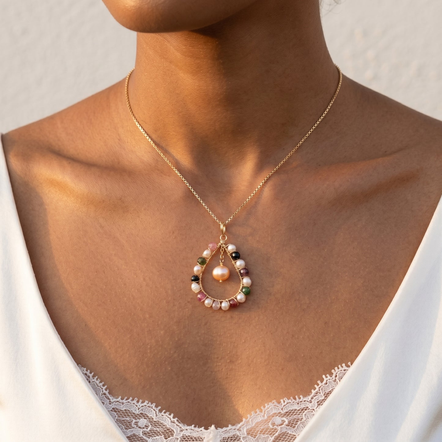 Necklace with a pendant featuring pearls and gemstones on a person wearing a white lace garment.