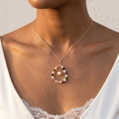 Necklace with a pendant featuring pearls and gemstones on a person wearing a white lace garment.