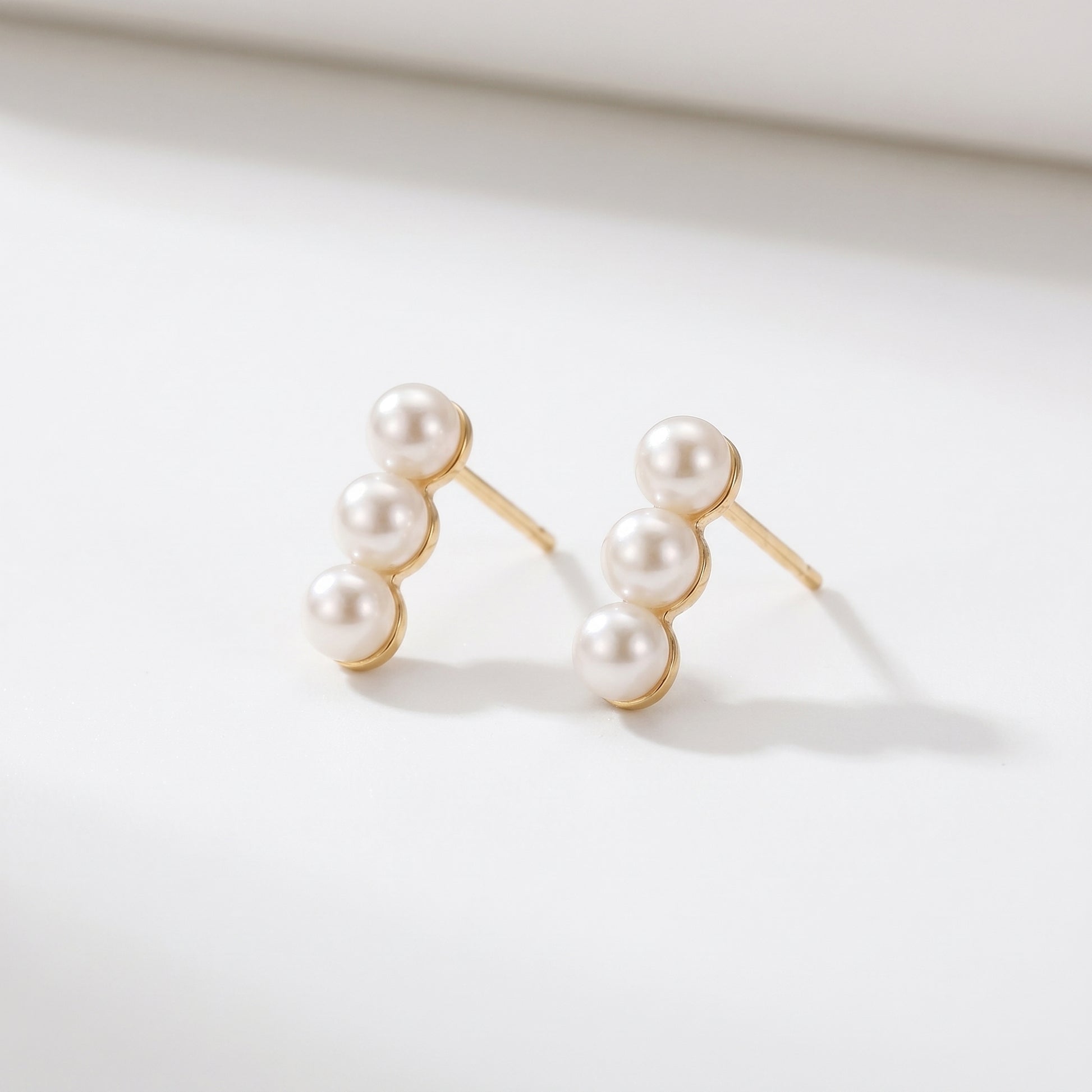 Pair of Lumina Trio delicate gold earrings featuring three vertical pearls on a clean white background.