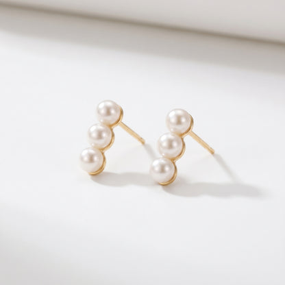 Pair of Lumina Trio delicate gold earrings featuring three vertical pearls on a clean white background.