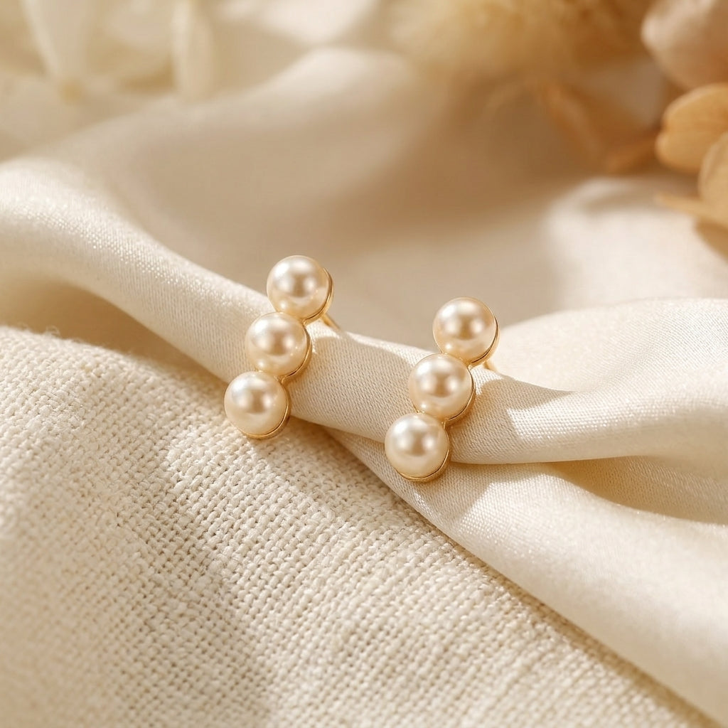 Lumina Trio natural freshwater pearl linear earrings resting on soft beige fabric.