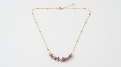 Gold necklace with purple beads on a white background