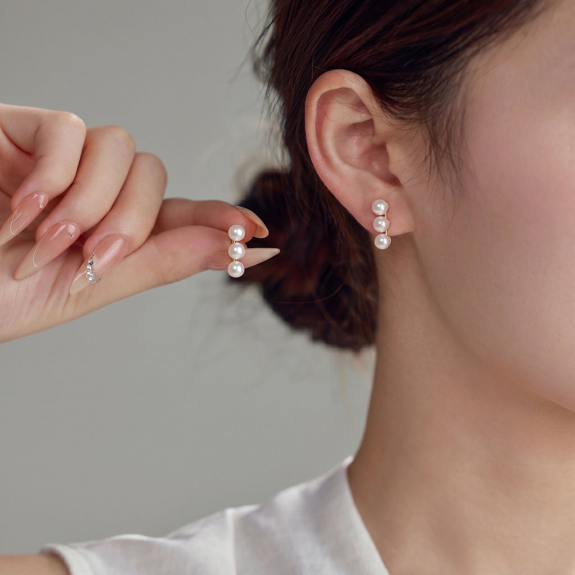 Close-up of a woman styling the elegant Lumina Trio pearl drop earrings with hair pulled back.
