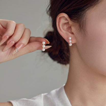 Close-up of a woman styling the elegant Lumina Trio pearl drop earrings with hair pulled back.