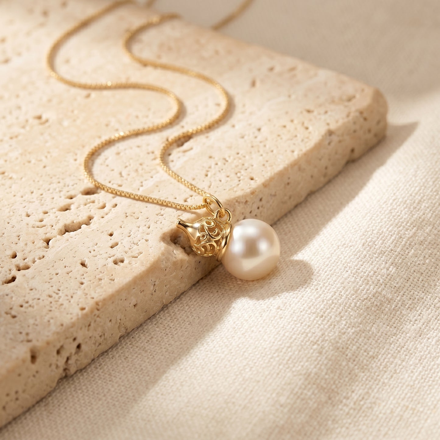 Gold necklace with a pearl pendant on a textured beige surface