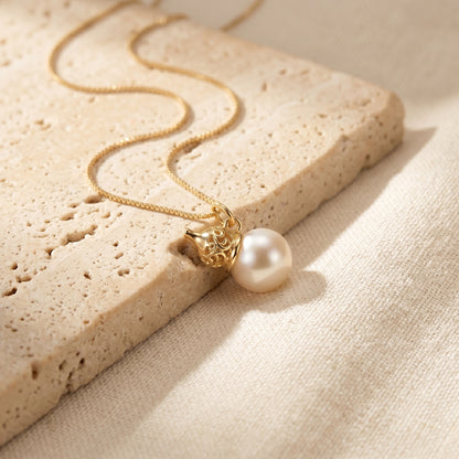 Gold necklace with a pearl pendant on a textured beige surface