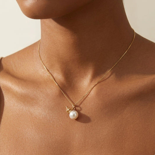 Gold necklace with a pearl pendant on a person's neck against a neutral background