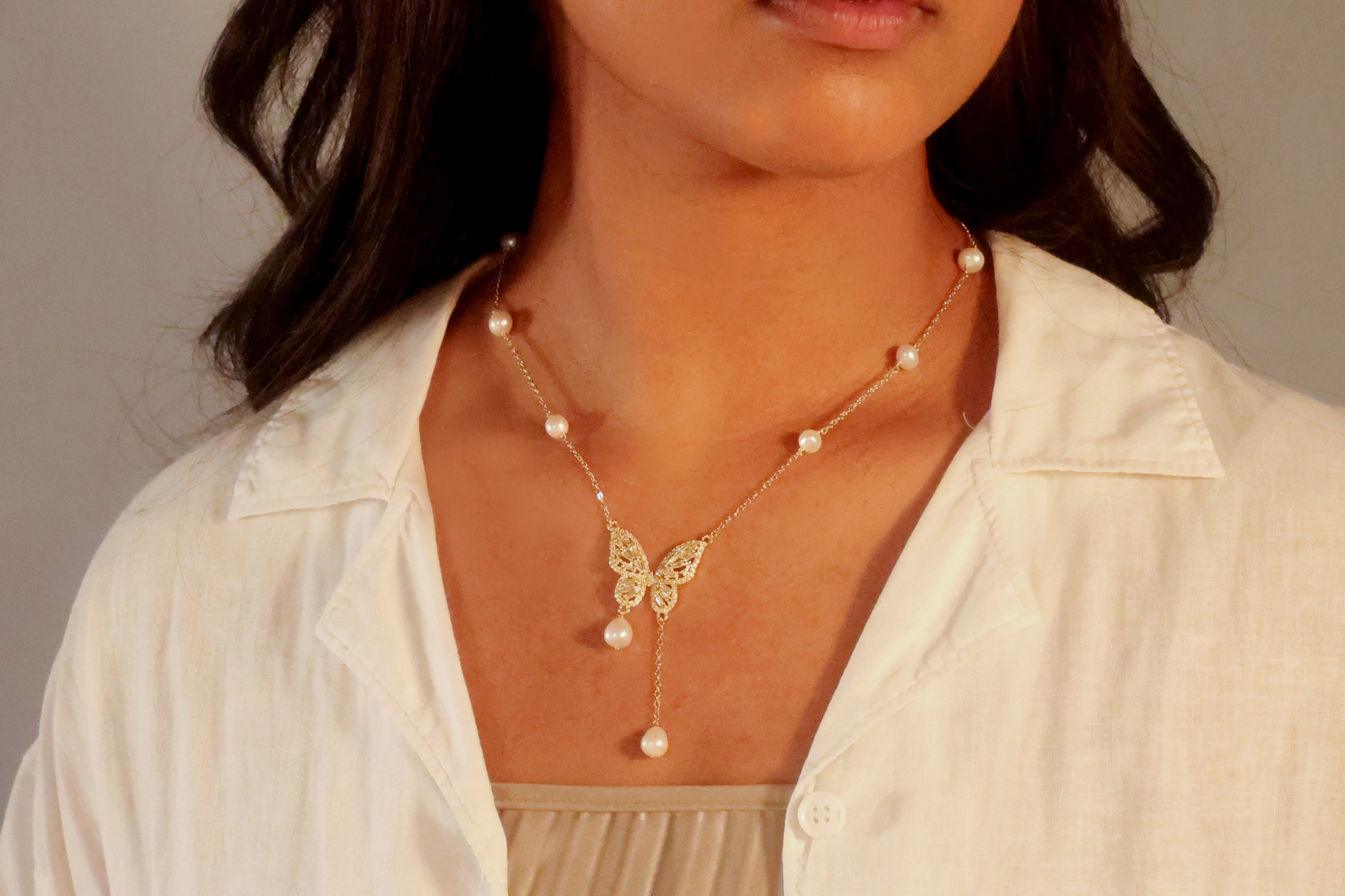 Woman wearing a romantic white dress and the dainty gold butterfly pearl drop necklace, wedding guest jewelry