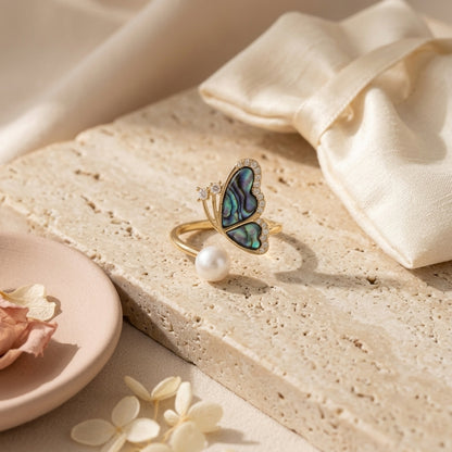Aura Abalone Butterfly Ring with natural pearl displayed on a textured stone tray with silk and dried flowers, highlighting its nature-inspired aesthetic by Whisperland Studio