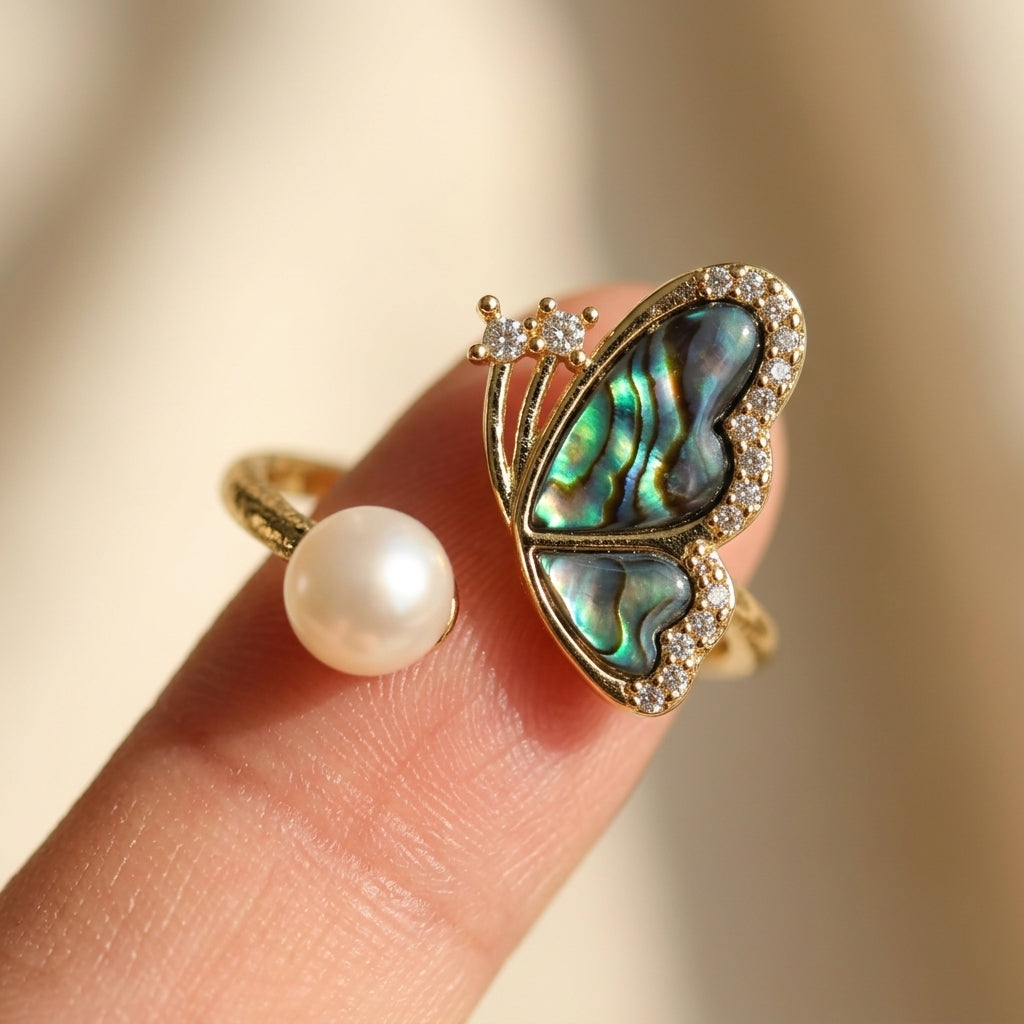 Close-up detail of the Aura Abalone Butterfly Ring on a finger, highlighting the iridescent green and blue shell patterns and the lustrous freshwater pearl by Whisperland Studio