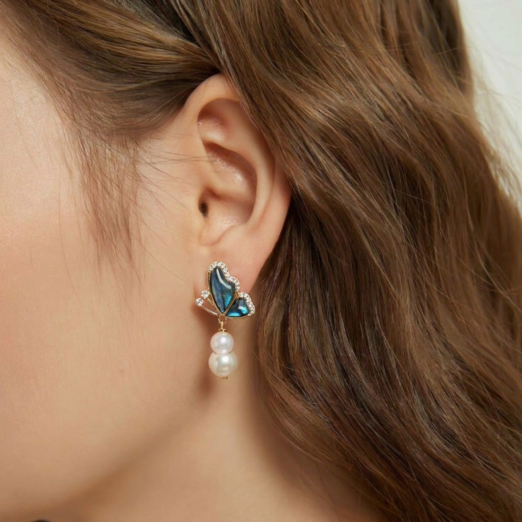 Model wearing Aura Papillon 14K gold plated earrings with abalone shell butterfly and baroque pearl drops.