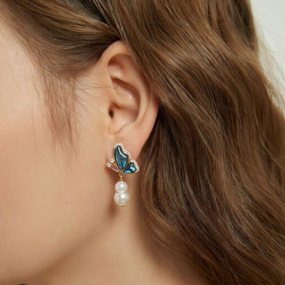 Model wearing Aura Papillon 14K gold plated earrings with abalone shell butterfly and baroque pearl drops.