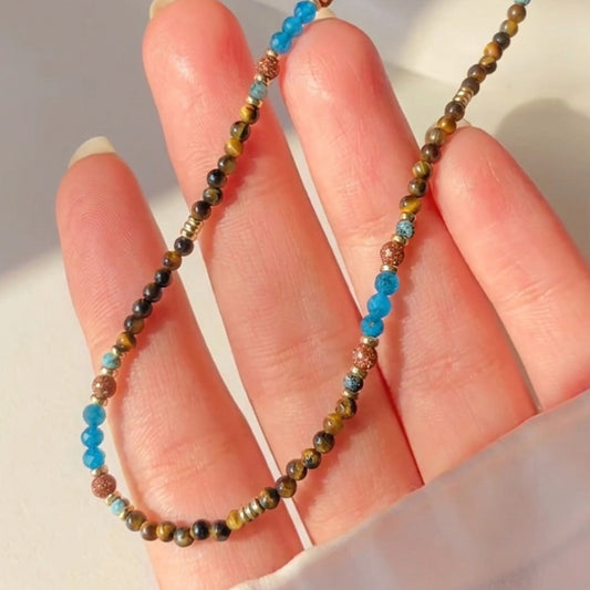 Close-up of handmade Terra Aura necklace showing genuine blue apatite and tiger's eye beads resting on a hand.