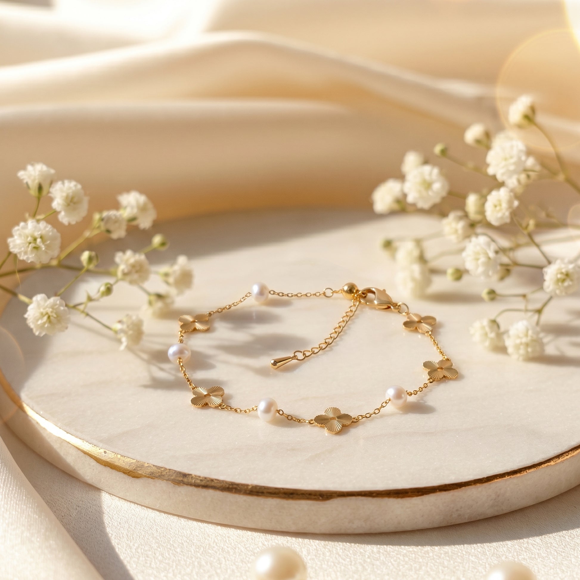 Dainty 14K gold pearl bracelet draped elegantly over soft cream silk fabric with tiny baby's breath flowers.