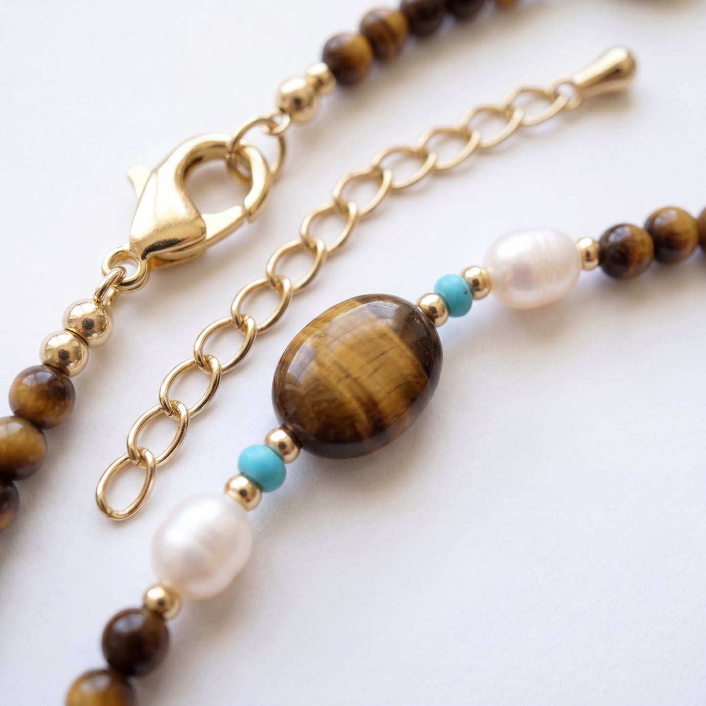 Necklace with brown tiger eye, white pearl, and turquoise beads on a gold chain.