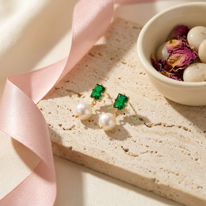 “Eden’s Whisper” Emerald and Freshwater Pearl Drop Earrings displayed on a textured stone surface with a pink ribbon