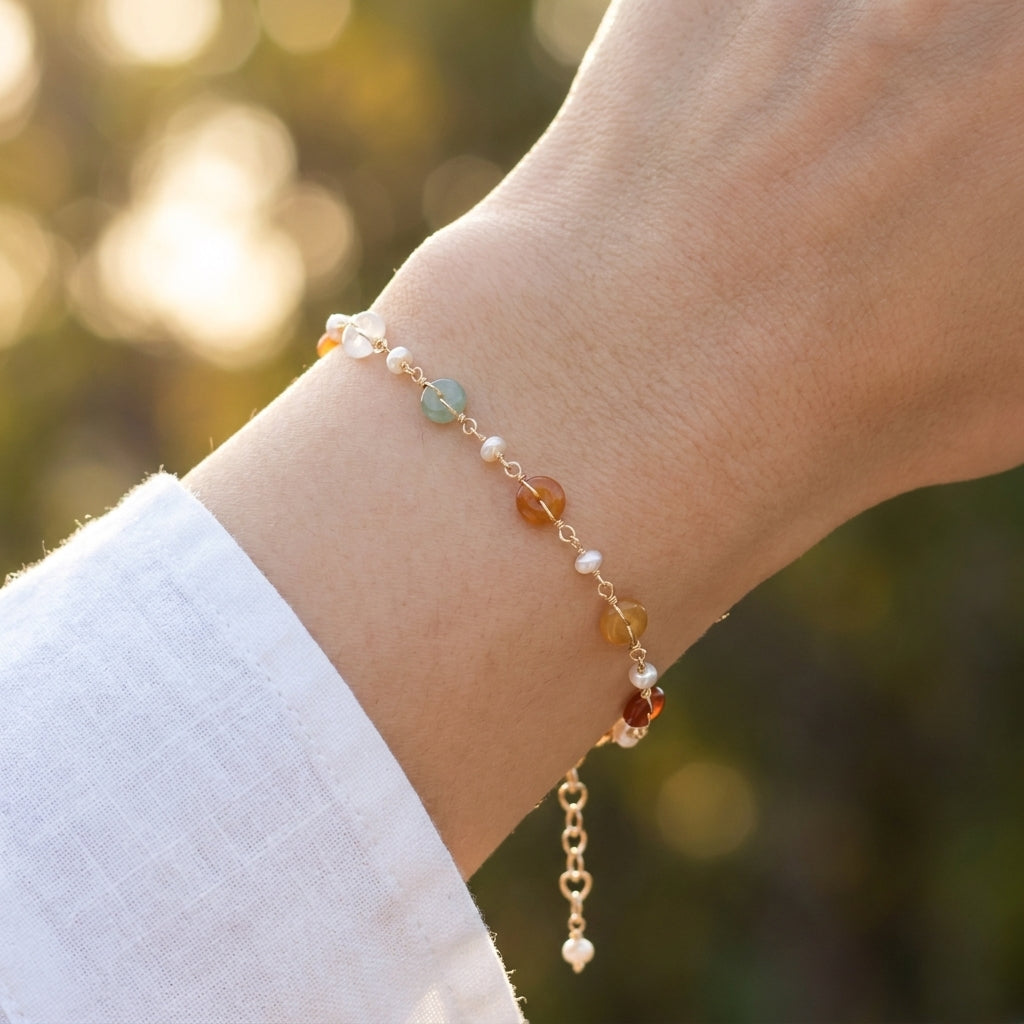 Close up of a woman's wrist wearing the Elara dainty 14K gold plated bracelet with freshwater pearls and green aventurine over a creamy linen fabric.