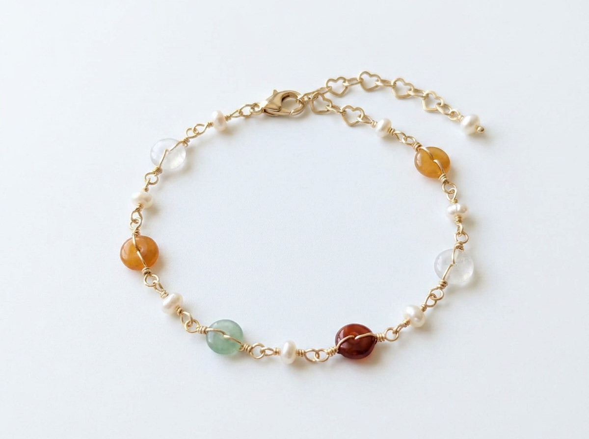 Delicate 14K gold plated Elara bracelet with colorful tourmaline, pearls, and green aventurine draped over a beige ribbed stone prop.