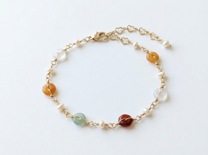 Delicate 14K gold plated Elara bracelet with colorful tourmaline, pearls, and green aventurine draped over a beige ribbed stone prop.
