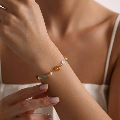 A hand wearing the minimalist Elara freshwater pearl and green aventurine bracelet resting against a soft tan background, showcasing everyday wear.