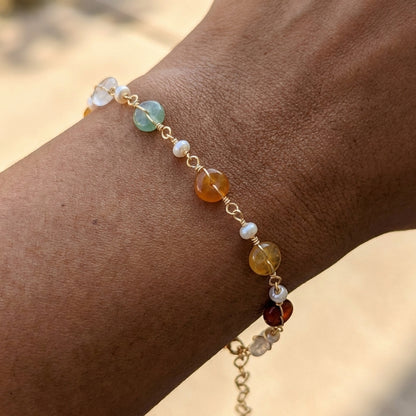 A hand wearing the minimalist Elara freshwater pearl and green aventurine bracelet resting against a soft tan background, showcasing everyday wear.