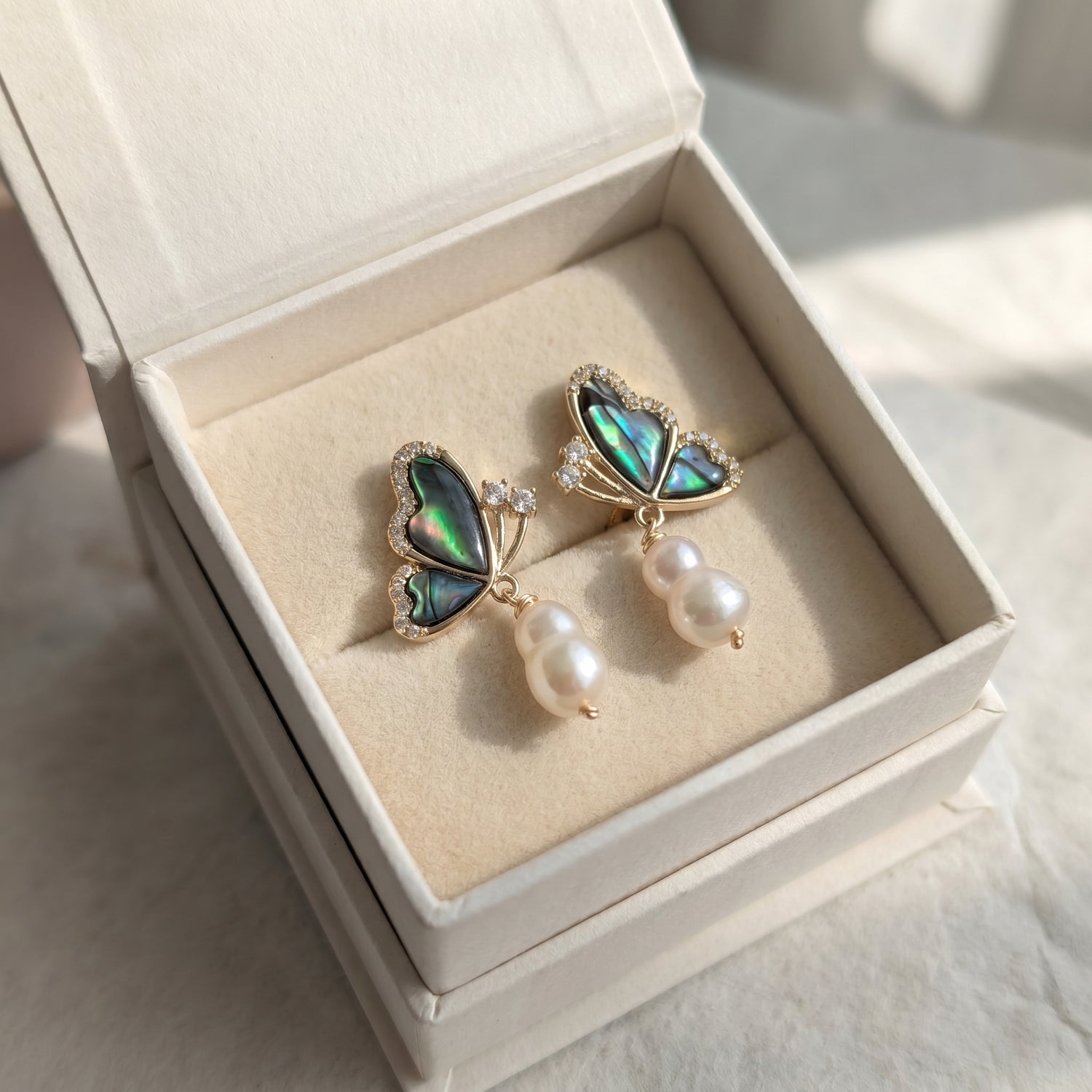 Butterfly-shaped earrings with green iridescent wings and pearl details in a jewelry box.