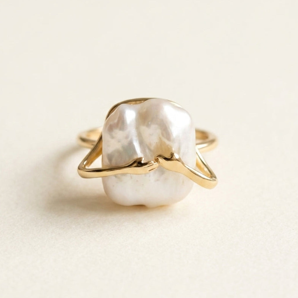The 'Embrace' 14K gold plated sculptural pearl ring displayed on a textured stone by Whisperland Studio.