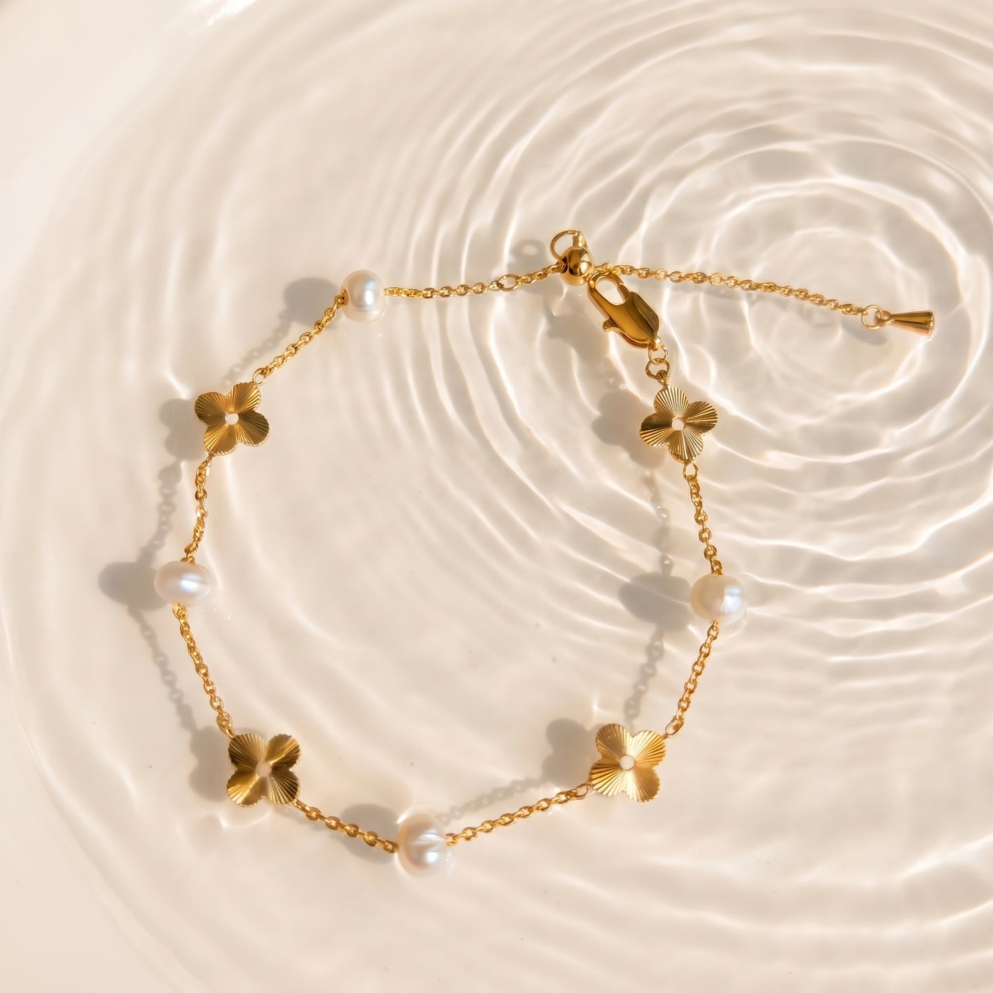 Flat lay of the Flora Whisper gold and pearl bracelet gently coiled on a creamy linen texture.