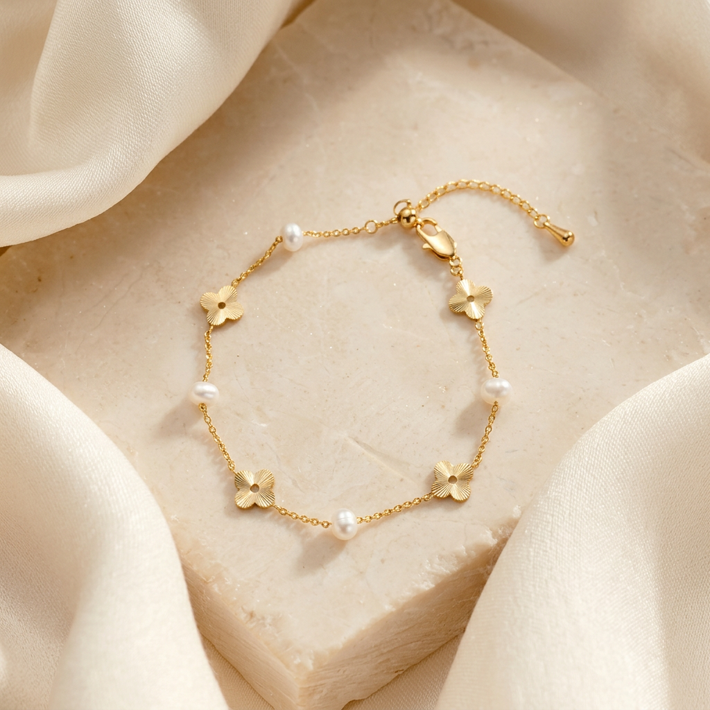 The Flora Whisper 14K gold and natural freshwater pearl floral bracelet elegantly displayed on a textured stone block draped with soft cream silk.