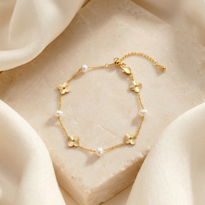 The Flora Whisper 14K gold and natural freshwater pearl floral bracelet elegantly displayed on a textured stone block draped with soft cream silk.