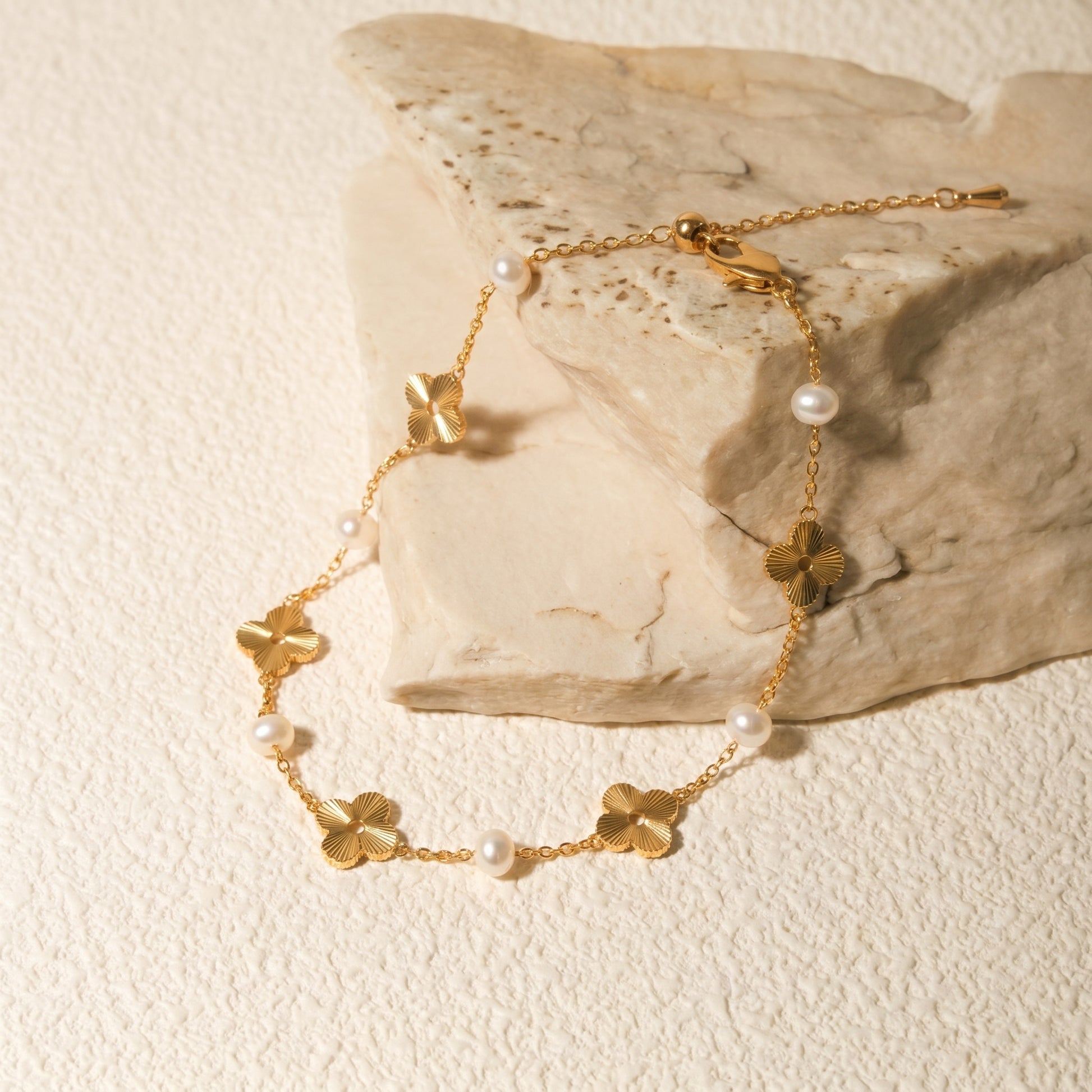 Woman's wrist wearing the Flora Whisper 14K gold and freshwater pearl floral bracelet resting on a textured plaster background.