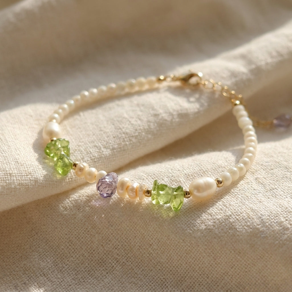 Pearl bracelet with green and purple gemstones on a beige fabric background