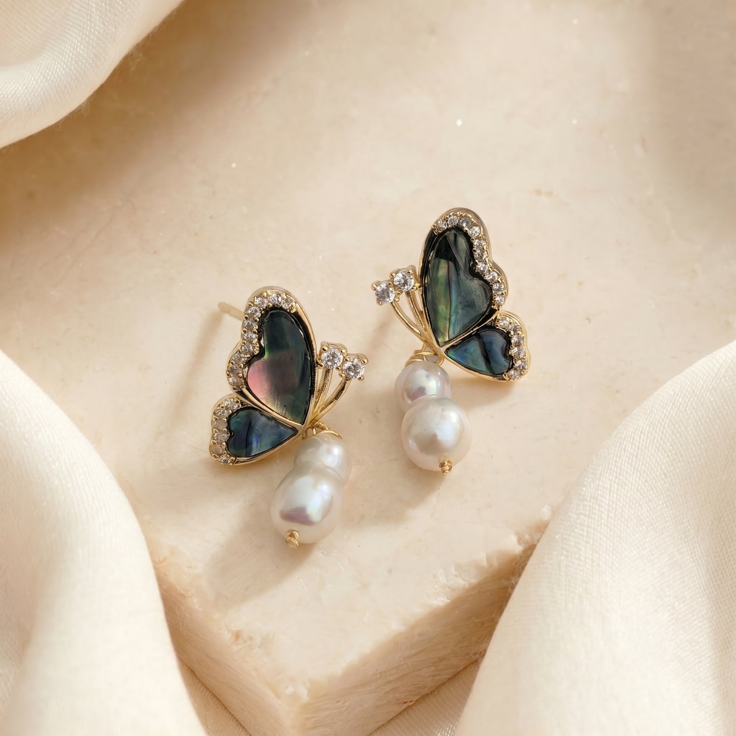 Flat lay of 14K gold plated butterfly earrings highlighting the iridescent green and blue abalone shell.