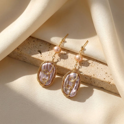 Macro detail shot of the classic round pearl and iridescent purple oval gemstone in a gold-plated setting.