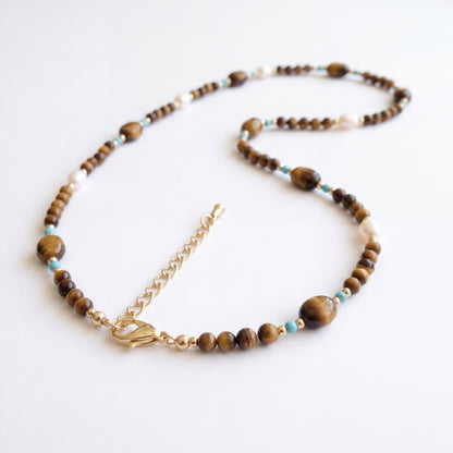 Tierra choker showing natural tiger's eye, turquoise, natural baroque pearls, and an 18K gold clasp on white.