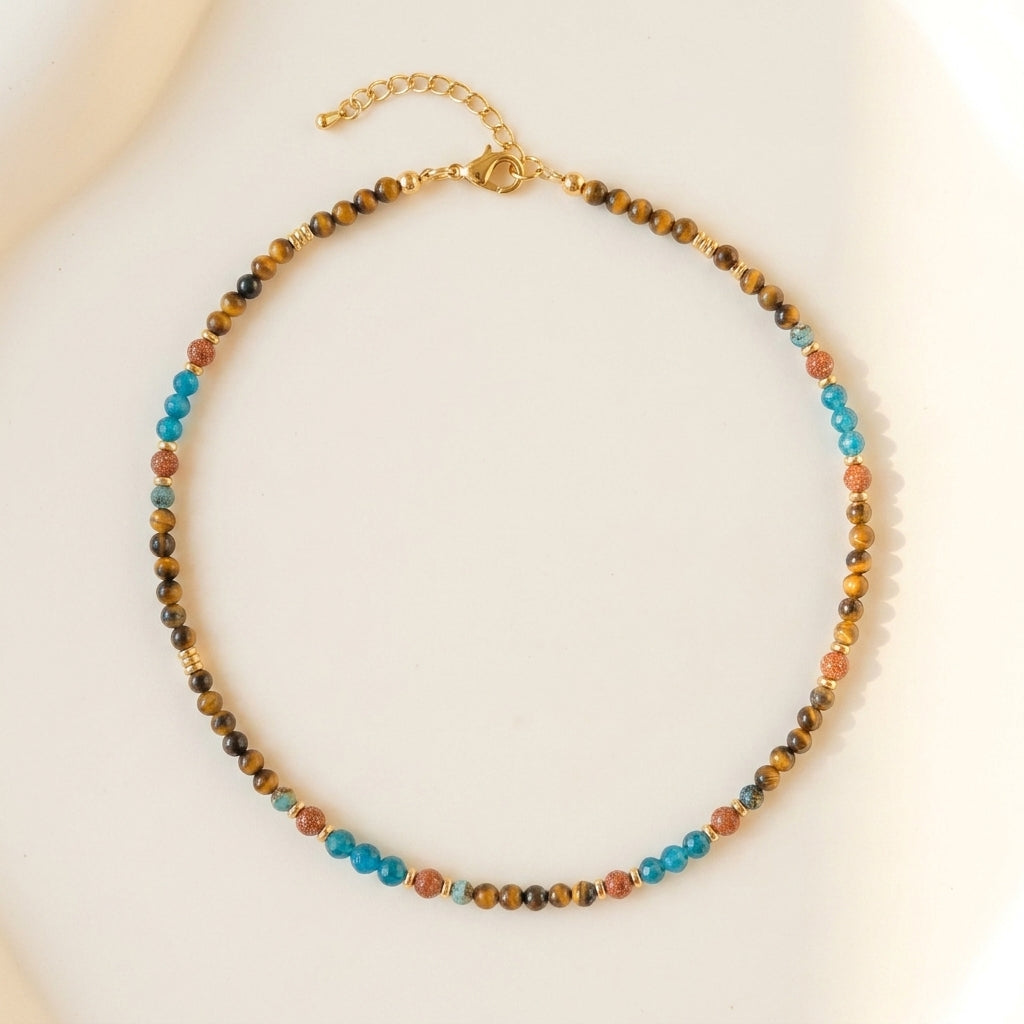 Artisanal gemstone choker featuring natural tiger's eye, blue apatite, and sandstone held delicately by hand.